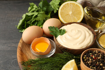 Board with bowl of mayonnaise and ingredients for cooking on dark wooden background