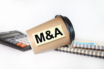 M&A. Mergers and acquisitions, text on sticker. The sticker is glued to a disposable coffee cup.