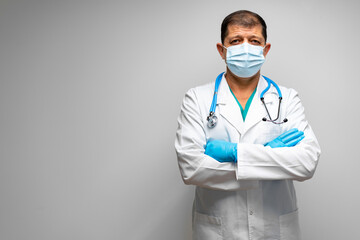 Senior male doctor in face mask standing against grey background