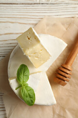 Baking paper with camembert cheese, basil and dipper on wooden background