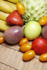 Tropical fruits on bamboo table. Atemoya(pineapple sugar apple),  banana, cherry tomatoes, passion fruits, sugar apples and wax apples on white background. Concept for harvest, vitamins,  health.
