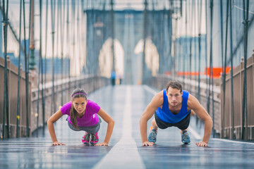 Fitness athletes training outdoors doing push-ups exercises workout on Brooklyn Bridge, New York...