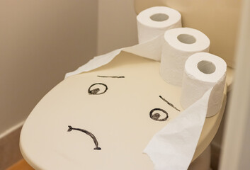 sad face on a toilet sit with toilet paper rolls 