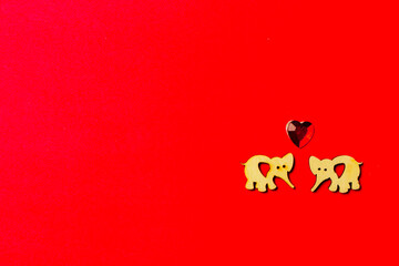 Two enamored wooden elephants with a crystal heart on a red background. Copy space. Valentine's day and wedding. Love postcard.