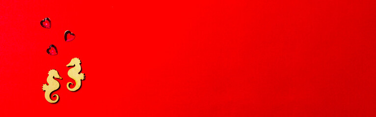 Two lovers wooden seahorses with a crystal heart on a red background. Long love banner. Valentine's Day and wedding concept.