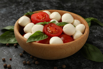 Bowl with mozzarella cheese, tomato and basil on black smokey background, close up
