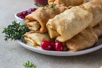 Homemade stuffed thin pancakes or crepes with meat, spicy cranberry sauce and arugula, light stone background. Traditional Russian cuisine for Maslenitsa. Shrove Tuesday.