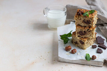 Oatmeal squares with chocolate and a cup of milk, light concrete background. Diet bars. Healthy bakery for breakfast or dessert.