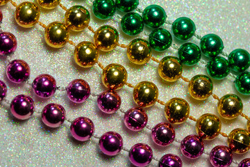 Macro defocused abstract view of traditional three-color Mardi Gras beaded costume jewelry necklaces on a sparkling white glitter texture background