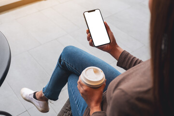 Mockup image of a woman holding mobile phone with blank white desktop screen while drinking coffee