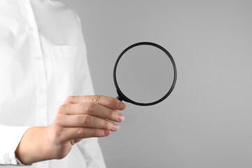Woman holding magnifying glass on grey background, closeup. Find keywords concept