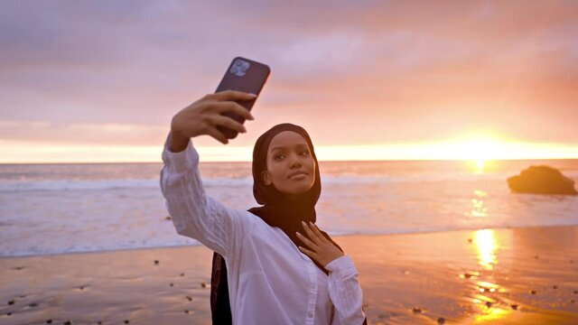 Somali-American woman taking a selfie at a beach in Malibut at sunset.