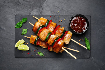 Delicious chicken shish kebabs with vegetables and sauce on black table, flat lay