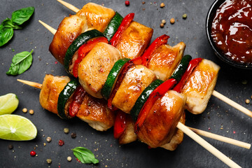 Delicious chicken shish kebabs with vegetables and sauce on black table, flat lay