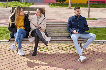 Two angry blonde girls sitting on a bench next to a boy. They are angry with the boy