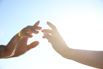 Man and woman reaching hands to each other against blue sky, closeup. Nature healing power