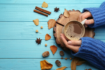 Woman with cup of hot drink at light blue wooden table, top view. Cozy autumn atmosphere