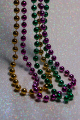 Macro defocused abstract view of traditional three-color Mardi Gras beaded costume jewelry necklaces on a sparkling white glitter texture background