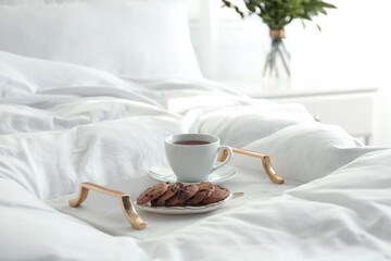Fototapeta na wymiar Cup of aromatic tea and cookies on soft blanket in bedroom