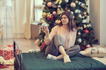 young woman sits on a bed against the background of a Christmas tree. concept of starting life anew after celebrations.