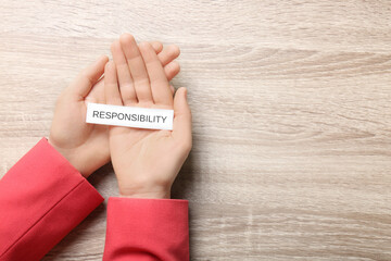 Woman holding card with word Responsibility at wooden table, top view