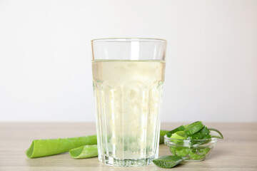 Fresh aloe drink in glass and leaves on wooden table
