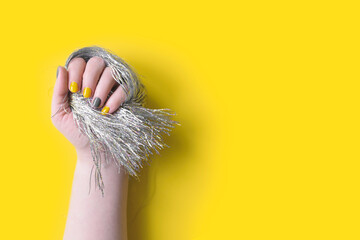 Detail of womans hand holding silver tinsel fringe with manicure