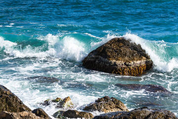 Turquoise sea stone beach, breaking waves in bright sunlight. Colorful bright sea background. The...