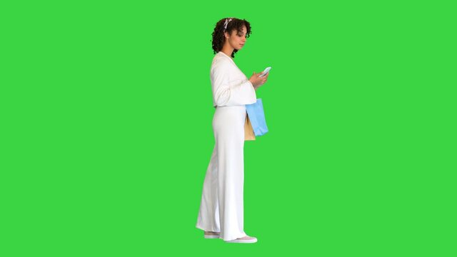 Young curly-haired lady with shopping bags using her smartphone on a Green Screen, Chroma Key.