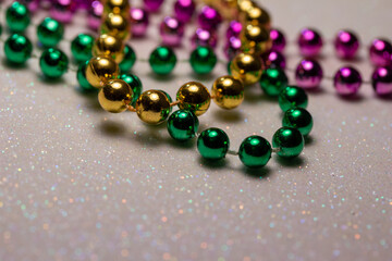 Macro defocused abstract view of traditional three-color Mardi Gras beaded costume jewelry necklaces on a sparkling white glitter texture background