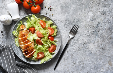 Baked chicken breast and salad with tomatoes on a concrete background. Healthy food, keto diet, paleo diet. Top view with copy space.