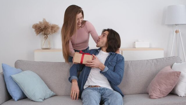 Young woman closing eyes of her boyfriend and giving him surprising gift, congratulation with holiday