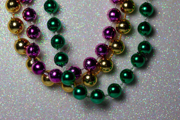 Macro defocused abstract view of traditional three-color Mardi Gras beaded costume jewelry necklaces on a sparkling white glitter texture background