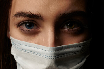 portrait of a crying girl in a medical mask close up. heterochromia
