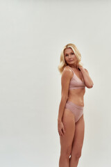 Fototapeta premium Looking good. Vertical shot of gorgeous middle aged caucasian blonde woman wearing lingerie posing isolated over grey background