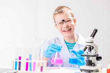 A schoolboy with a microscope examines chemicals in test tubes, conducts experiments - a portrait on a white background. Concept for the study of coronavirus in the laboratory