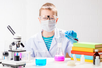 A schoolboy with a microscope and book examines chemicals in test tubes, conducts experiments - a portrait on a white background. Concept for the study of coronavirus in the laboratory