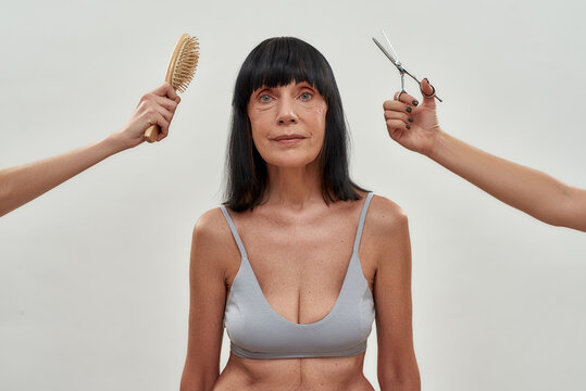 New Look. Two Hands With Hair Brush And Scissors Doing Haircut For A Senior Half Naked Woman, Isolated Over Grey Background