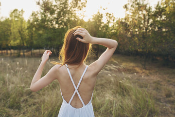 Obraz premium portrait of a happy woman in a sundress in a field year from behind trees sunset