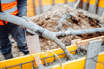 workers pouring concrete with concrete hose. Details of construction site and close up details of worker workwear