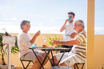 Mature and young family people enjoy time together with dirnks and food outdoor at home - concept of grandfathers and grandson enjoy and have fun on vacation