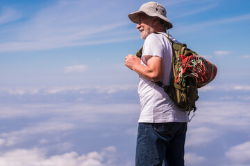 Active old senior man enjoy the freedom and nature travel alternative backpack style stand up with blue sky and clouds in background - youthful old mature people enjoy trekking and healthy lifestyle