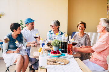 Group of friends mixed ages adult and senior have fun together enjoying food and drinks around a table at home - celebration and cheerful caucasian people with different generations