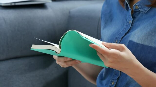 Relax asian woman reading book sitting on sofa in living room holding book to read. Young woman relaxation reader reading open book leisure mind. Happiness beauty woman person smiling face happy time