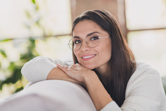 Photo of cheerful girl sit sofa rest head arms beaming smile wear eyeglasses white sweater in living room home indoors