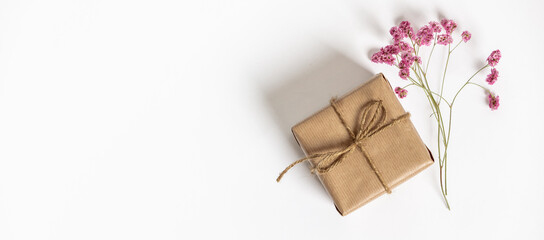 Gift box wrapped in kraft paper and pink flowers on white background. Flat lay styling.