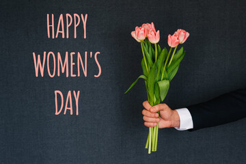 Bouquet of pink tulips in a man's hand. Greeting card with text Happy Women's day