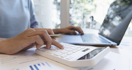Financial or accounting professionals use a laptop to analyze the company's revenue-expenses graph to prepare for presentation to the chief executive and partner, businesswomen working in the room.