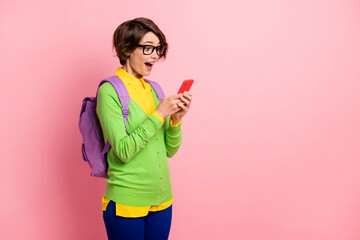 Photo of impressed woman wear green cardigan spectacles rucksack looking gadget empty space isolated pink color background