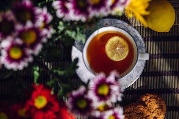 Top view cup of tea with lemon through purple blurred flowers.
